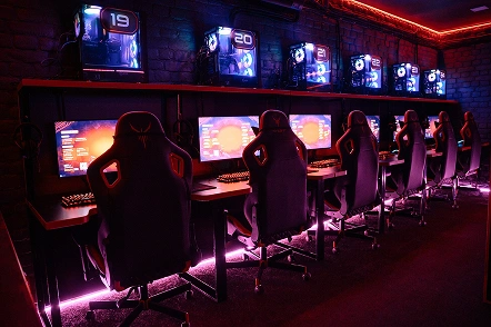 Een rij professionele gaming-pc's en computerstoelen met rode neonverlichting in een internetcafé of e-sports arena.
