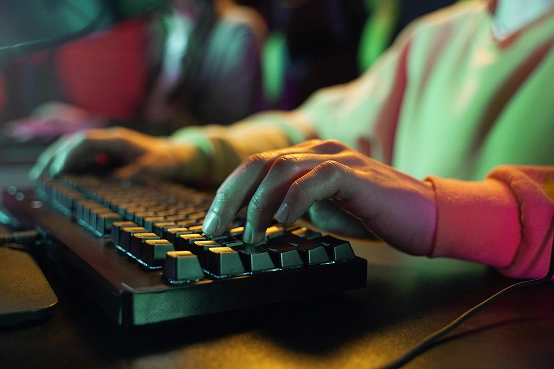 Close-up van de handen van een gamer die typt op een mechanisch toetsenbord onder sfeervolle gekleurde verlichting.