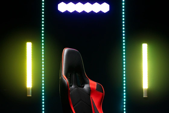 Een zwart-rode ergonomische gamingstoel in een donkere kamer verlicht door neon LED-strips aan de muur.